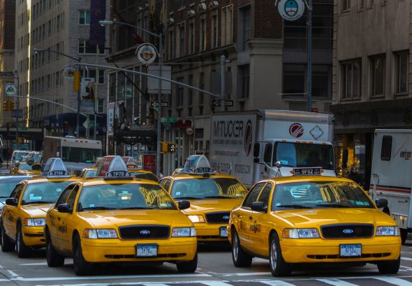 yellow taxi cab on road near white concrete building during daytime